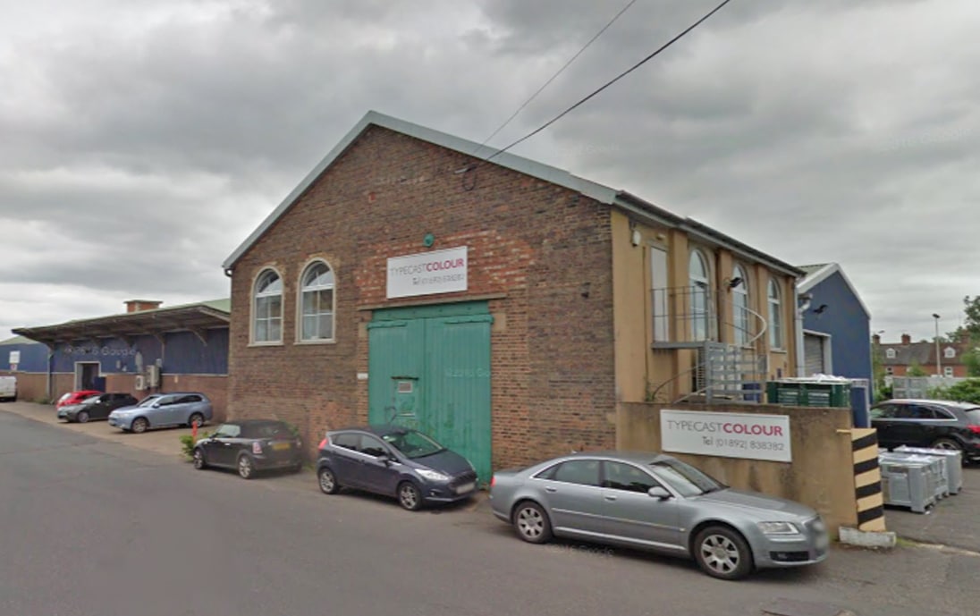 Exterior view of a red brick industrial building featuring green double doors and Typecast Colour signage